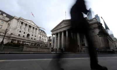 Person walking past Bank of England building, gloomy sky.