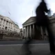 Person walking past Bank of England building, gloomy sky.