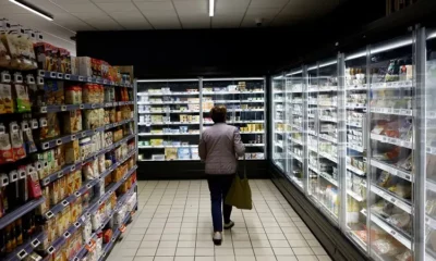 Person shopping in a supermarket aisle with freezers.