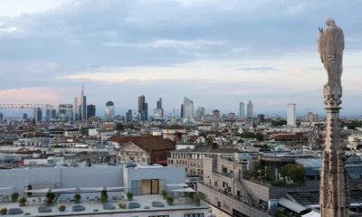 Milan skyline with statue foreground, cloudy sky.