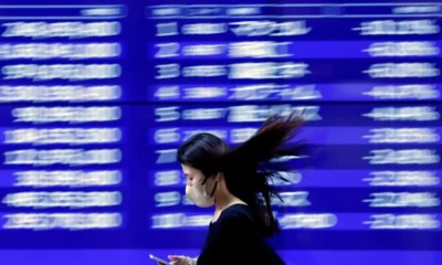 Woman with phone passing blurred flight information board.