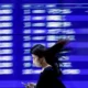 Woman with phone passing blurred flight information board.