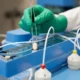 Gloved hand holds pill with tweezers in laboratory.