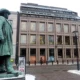 Statue outside modern building in snowy urban setting.