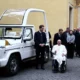 Pope in wheelchair beside popemobile.