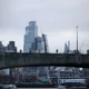 City skyline view with bridge foreground, cloudy sky.