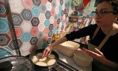 Woman frying dough in kitchen with colourful tiles.