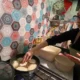 Woman frying dough in kitchen with colourful tiles.