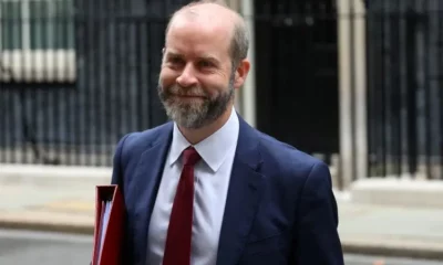 Man in suit holding red folder, smiling.