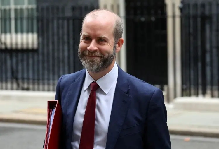 Man in suit holding red folder, smiling.