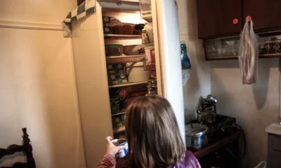 Child holding can in front of open fridge.