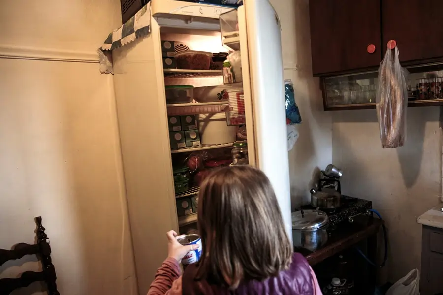 Child holding can in front of open fridge.