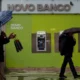 People with umbrellas walking past Novo Banco ATMs.