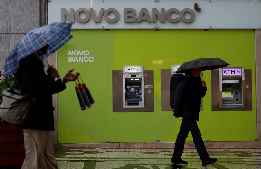 People with umbrellas walking past Novo Banco ATMs.