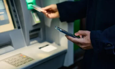 Person using ATM, holding phone and card.