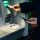 Person using ATM, holding phone and card.